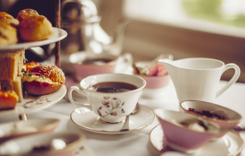 Table set for afternoon tea, tray of tea sandwiches and pastries, cups of tea.